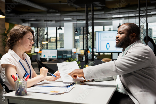 HR manager and job seeker discuss personal and professional benefits package such as salary, rights and other onboarding terms. Reviewing CV and contract document in a corporate setting.