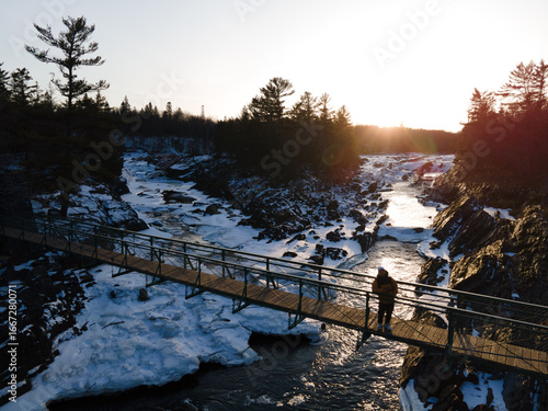 Couple on the suspension bridge looking at the sunset on a winter landscape in Minnesota