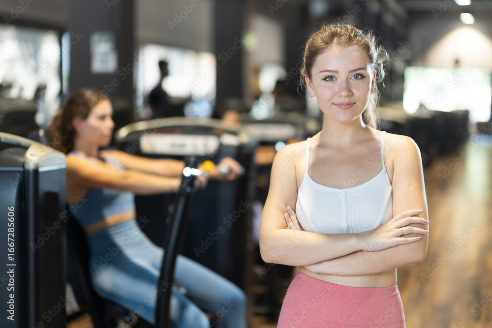 Fototapeta premium Glad young woman posing against background of professional training machines in fitness studio
