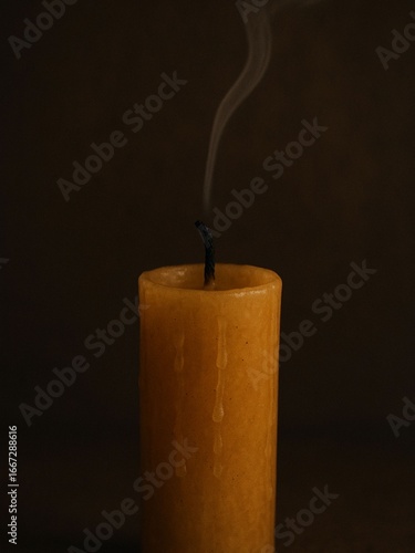 Yellow candle just extinguished with smoke on dark background