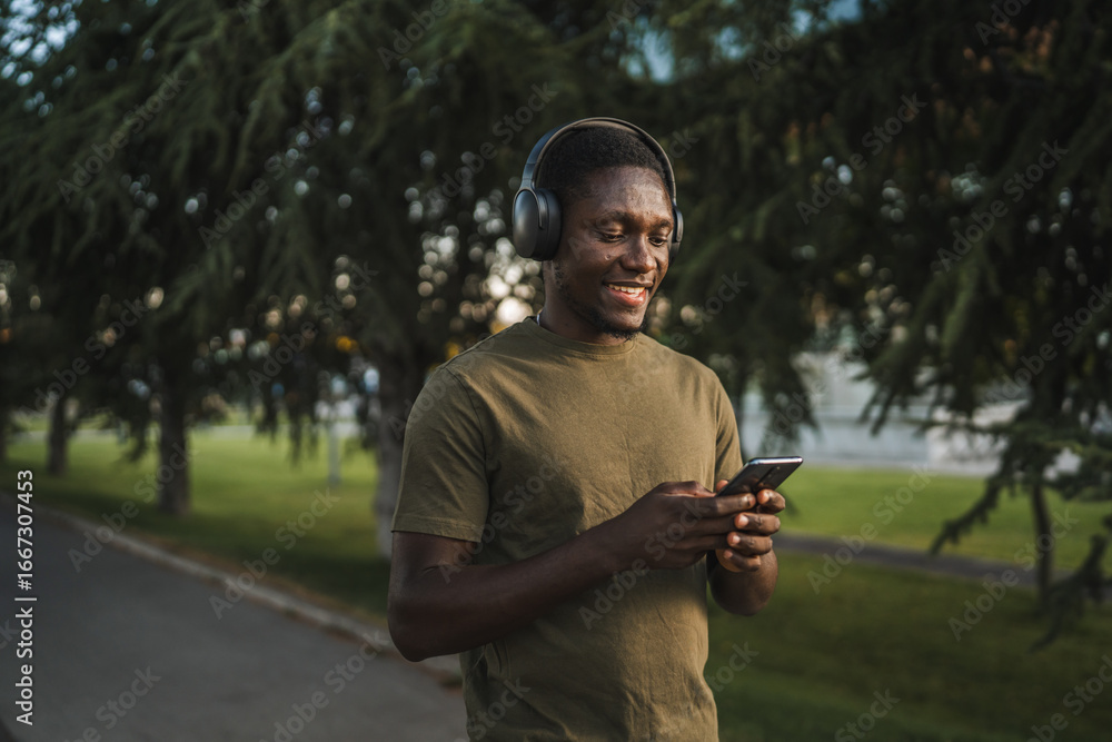 Obraz premium Young man wearing headphones listening to music on smart phone in park