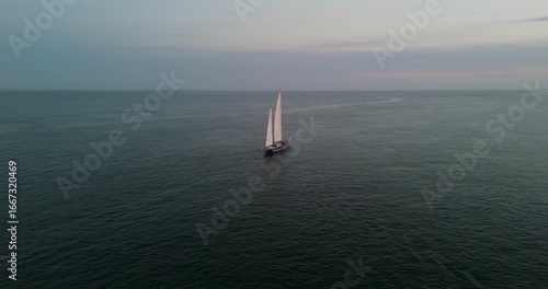 Classic sailboat navigating calm ocean waters during sunset
