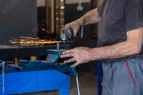 The locksmith cuts off the metal, clamped in a vice, with a grinder with a cut-off wheel. Sparks from metal polishing by the grinder.