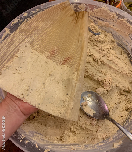 Spreading masa on corn husks to make tamales, traditional mexican food for holidays and celebrations.