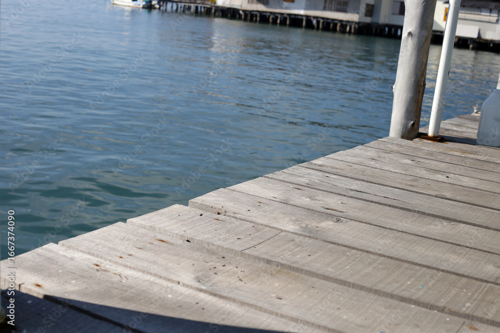 Fototapeta premium Wooden pier planks extending over calm blue water.