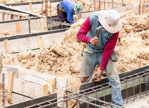 Fototapeta Construction worker hammering wooden formwork with rebar reinforcement