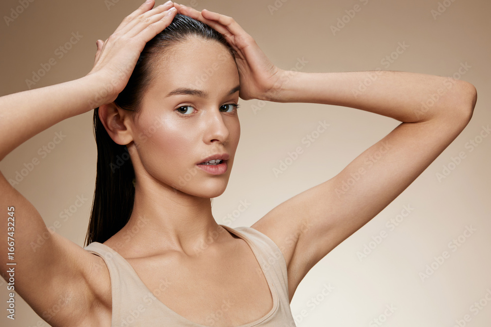 Naklejka premium Young woman with long hair holding her head, showcasing healthy hair and skin on a neutral background, exuding calmness and confidence