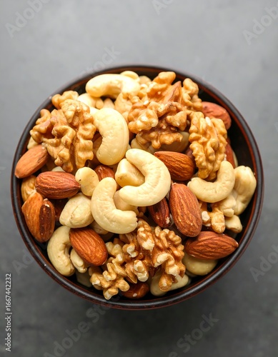 A dark bowl brimful of almonds, cashews, and walnuts sits on a grey surface