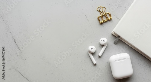 Minimalist flat lay of modern workspace with wireless earbuds notebook and copy space on a grey marble background.