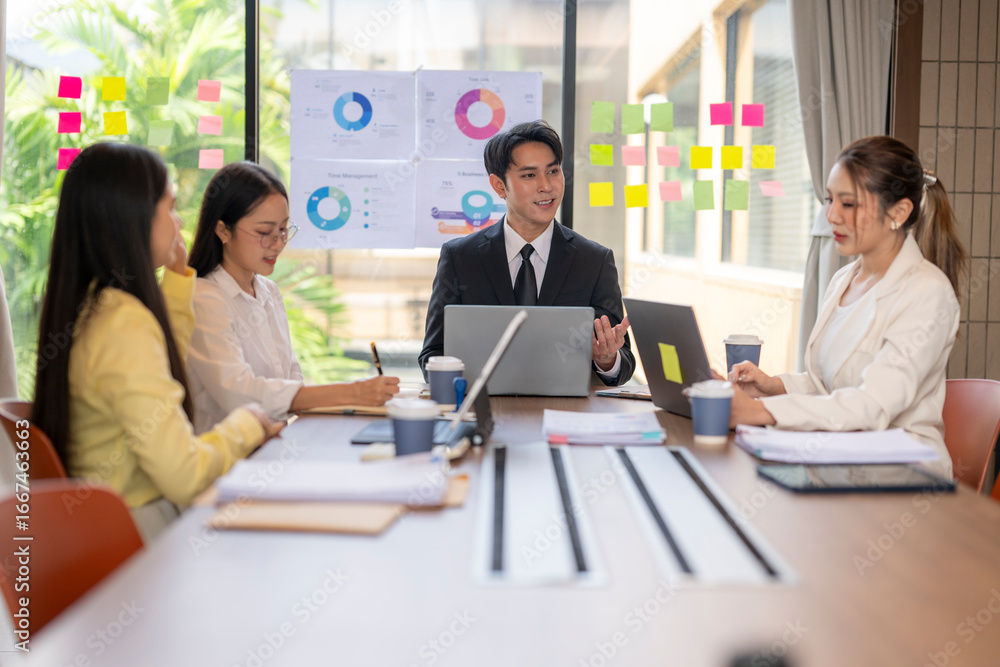 Business team meeting in modern office analyzing charts on sticky notes and laptops Business team meeting in modern office analyzing charts on sticky notes and laptops