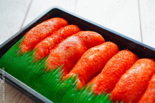 Fresh pack of mentaiko salted cod roe neatly arranged in a black tray with green divider, Japanese seafood delicacy, closeup detail.