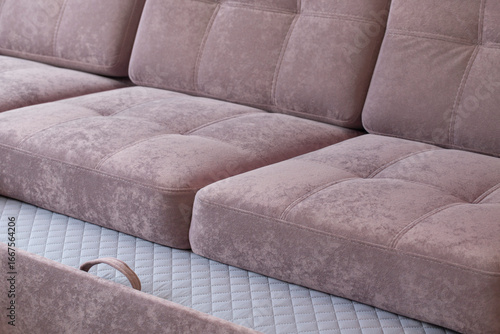 Pink quilted sofa made of shaggy velour fabric with pull-out bed. Soft furniture for relaxation made of plush material and loop for transformation into a place to sleep.