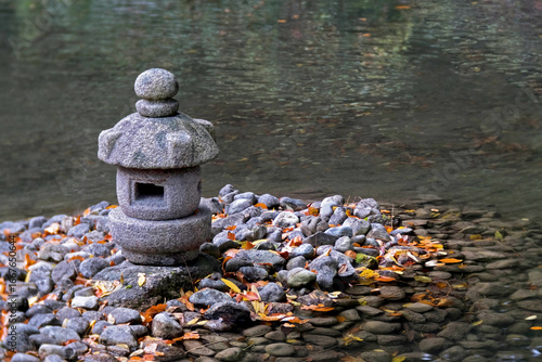 Small Asian decorative stone temple in a pond surrounded by autumn leaves shimmering in the water