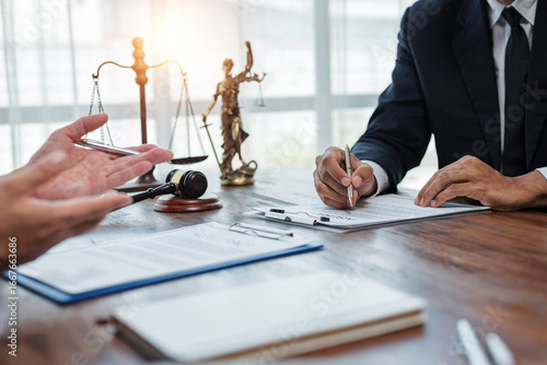 Lawyer and client discussing terms and conditions while signing legal document in office with gavel and justice scales in background
