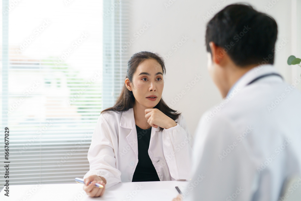 Two Asian doctors engaged in a discussion during a meeting in the hospital office, focusing on patient care and treatment strategies Two Asian doctors engaged in a discussion during a meeting in the hospital office, focusing on patient care and treatment strategies