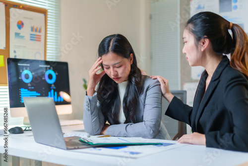 Businesswoman providing comfort to her stressed colleague dealing with a headache in a modern office environment, showcasing empathy and support