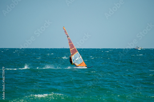 Wallpaper Mural A windsurfer with a transparent orange sail glides across deep blue-green waves under a clear sky, embracing the power of the wind. Torontodigital.ca