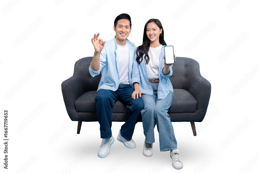 Obraz premium Happy couple smiling and showing mobile phone, ok gesture and sitting on couch. Couple with a phone smiling on PNG background