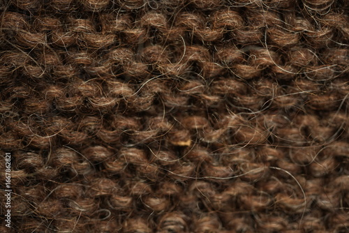 Dark brown wool knitted fabric texture, macro. Close-up view of warm, fuzzy wool yarn in a dense hand-knitted pattern. Natural textile structure with visible fibers and stitches