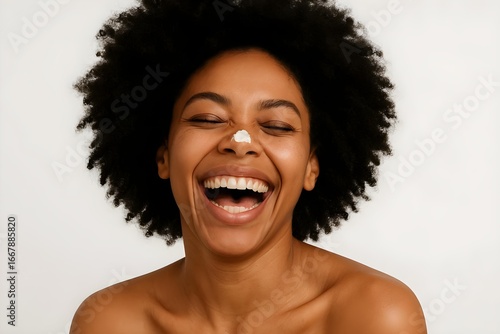 A woman with curly hair laughs joyfully, featuring a small amount of cream on her nose against a light background. Concept Joyful Laughter, Curly Hair, Playful Charm, Light Background, Creamy Detail