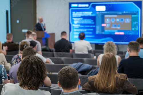 Audience listening to speaker presenting on large screen in professional business seminar setting