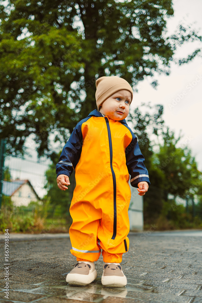 Fototapeta premium An adorable and cheerful toddler dressed in a bright orange rain suit joyfully playing outdoors during a rainy day, showcasing the pure bliss and innocence of childhood in the wet weather