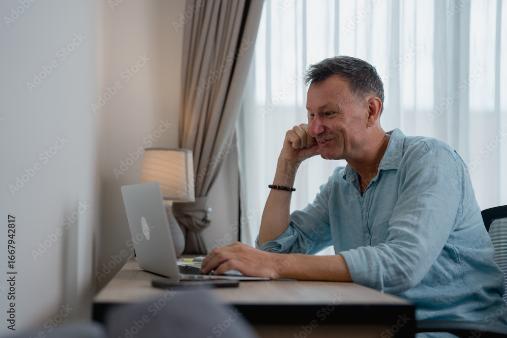 Naklejka premium Happy businessman sitting at desk using laptop computer working remotely from home office enjoying online meeting or reading good news on internet website