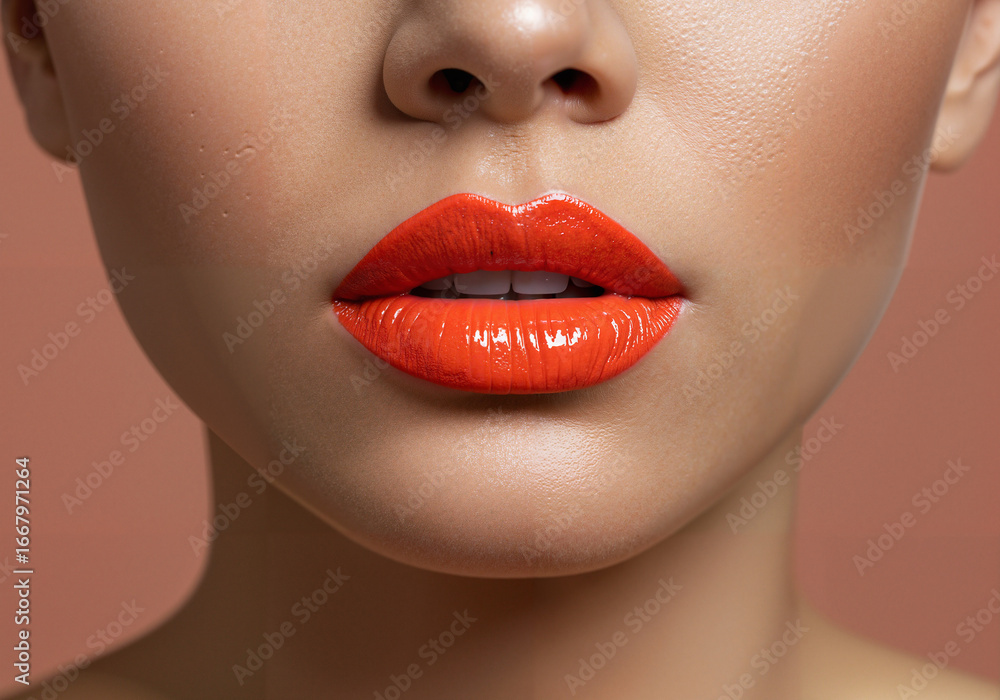 Obraz premium Close-up of woman’s lips with vibrant orange lipstick on peach background