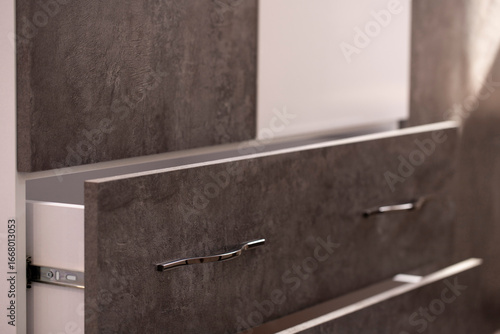 Close-up of the drawers of the cabinet with grey cement structure facades and white doors with curved silver handles, sliding on chromed guides. Furniture cabinet for storing things and accessories.
