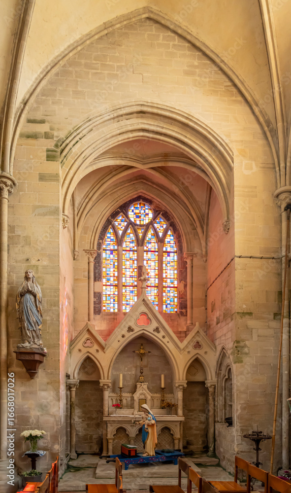 Fototapeta premium Langrune-Sur-Mer, France - 08 05 2025: Detail view of a chapel with a statue of the Virgin Mary and Chil, an altar and stained glass windows inside the Saint-Martin Church
