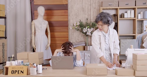 Adult asian daughter stressed holding head while senior mother checking order inside boutique fashion studio small family business teamwork e-commerce packaging quality control online shop