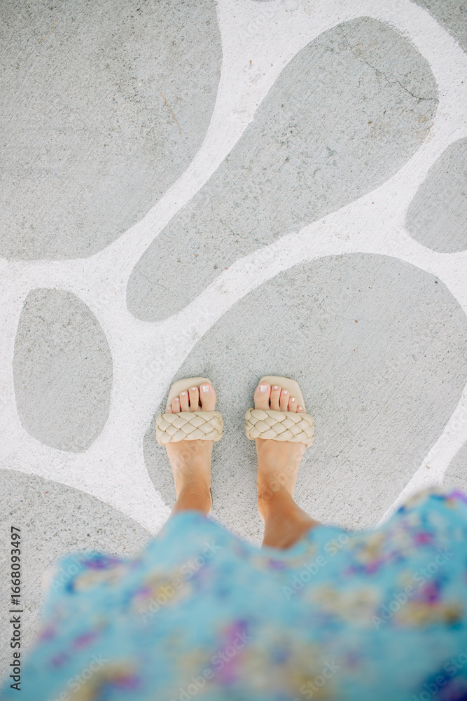 Naklejka premium Feet in Woven Sandals on Patterned Concrete