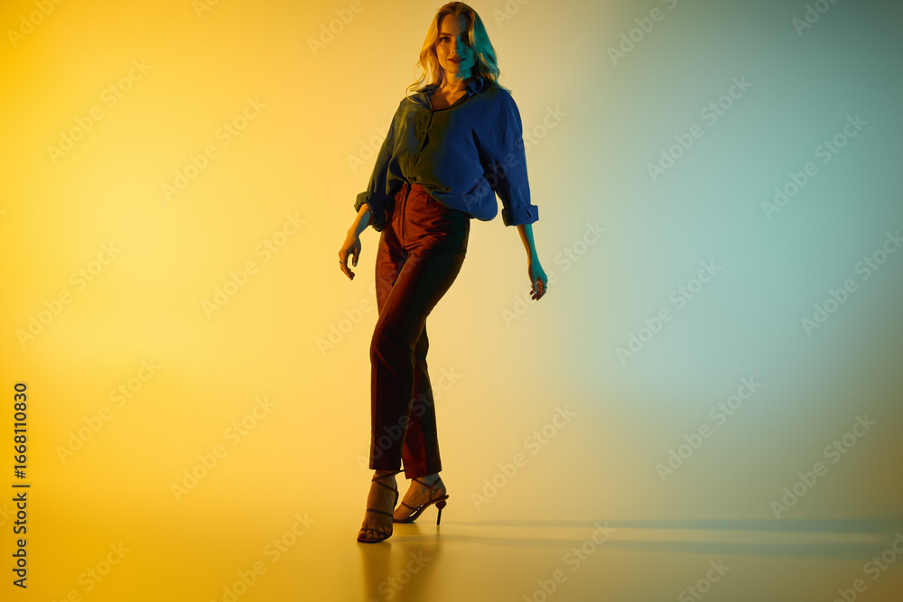 Fototapeta premium Stylish young woman poses confidently in trendy outfit against vibrant colored backdrop