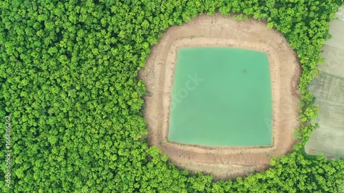 Aerial view of a square pond filled with turquoise water, contrasting against the surrounding lush green trees, Dinajpur, Rangpur Division, Bangladesh.