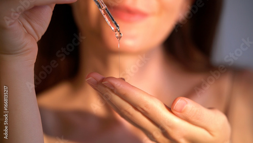Young woman holding a dropper with serum for face. Facial oil fall from a glass pipette, macro view. Selective focus. Cosmetic background with liquid skincare product, beauty concept. Dermatology