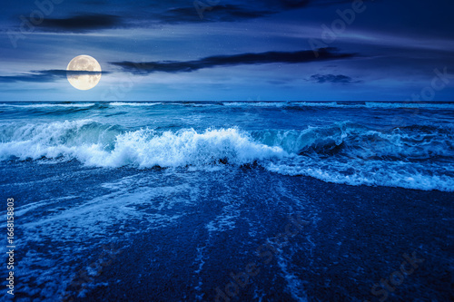sea tide before storm at night. wave splash with foam on wet sandy beach in full moon light. windy weather on velvet season. dramatic seascape background