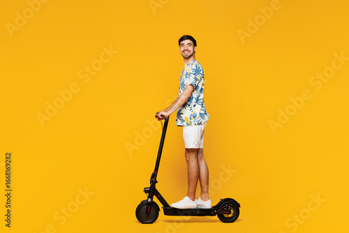 Full body side view young smiling happy Caucasian man he wear blue beach t-shirt casual clothes ride e-scooter look camera isolated on plain yellow orange background studio portrait Lifestyle concept
