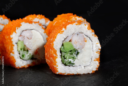 California uramaki sushi rolls with flying fish roe, shrimp, avocado and cucumber lying on a black slate plate