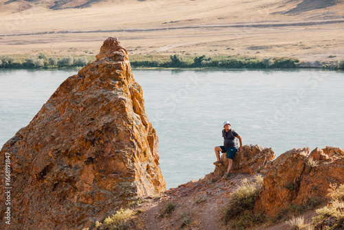 Bilde på lerret Hiker resting on rocky cliff enjoying view of Ili River flowing through arid lan