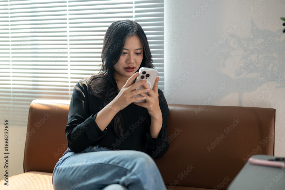 Obraz premium Young asian woman using smartphone while relaxing on sofa at home