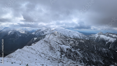 Snow-covered ridge and peaks of Tatra Mountains under dramatic cloudy sky in Poland.