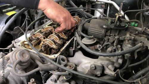 mechanic is conducting a manual tune-up on the rocker arm assembly of a car engine.
