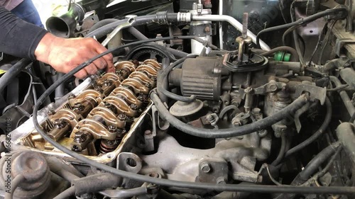 mechanic is conducting a manual tune-up on the rocker arm assembly of a car engine.