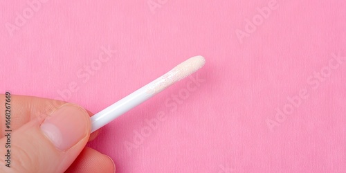 Close-up of a hand holding a cotton swab with a soft tip against a vibrant pink background, showcasing personal care and hygiene products in a minimalist setting