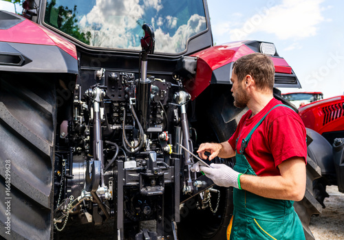 Male mechanic checking farm tractor using digital tablet in rural area