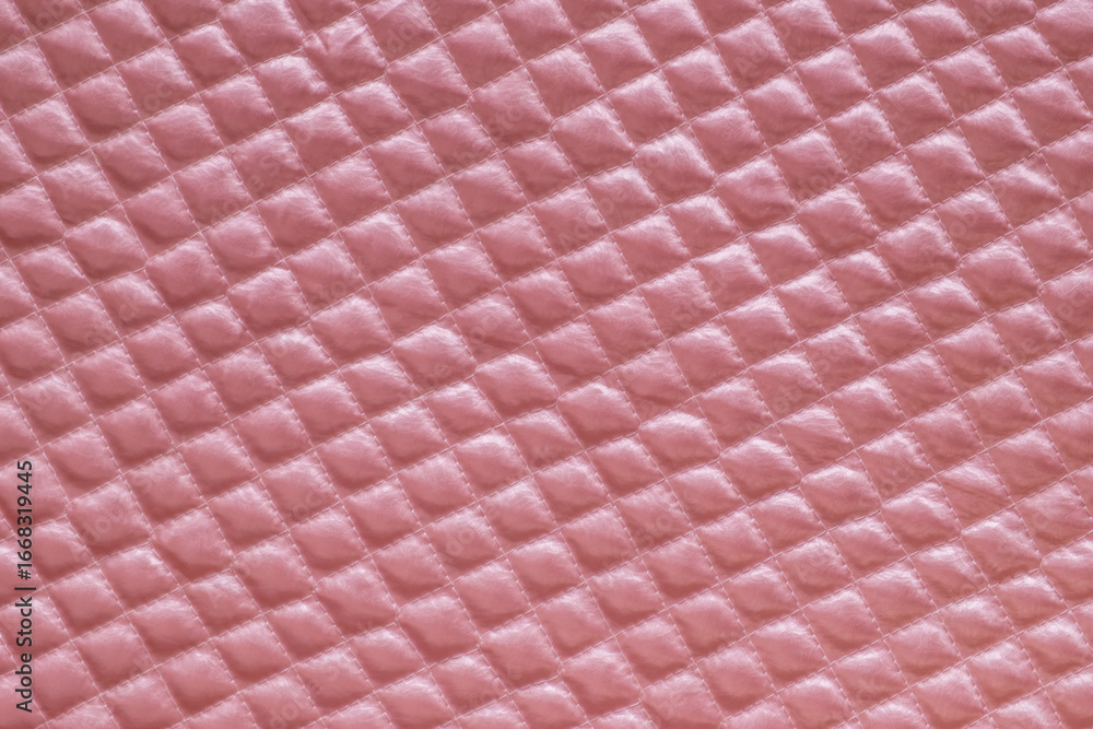 Naklejka premium Close-up of soft pink quilted fabric with a diamond pattern. Showcasing its plush texture and subtle sheen. Ideal for backgrounds or textile designs, conveying comfort and elegance.