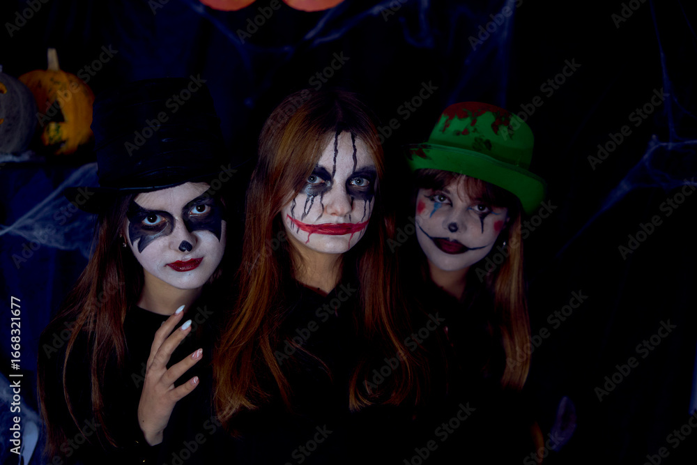 Obraz premium teenage friends with stage makeup mime during acting class celebrating Halloween in a dark room decorated with cobwebs and pumpkins with candles