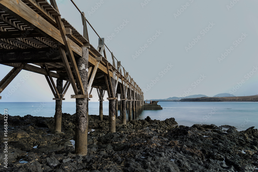 Fototapeta premium Old wooden pier stretching into the calm ocean at dusk