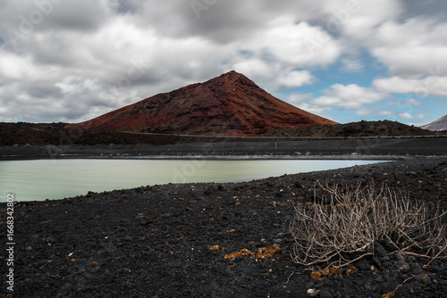 Volcanic landscape with a red mountain, a small pond and dry vegetation in lanzarote, canary islands