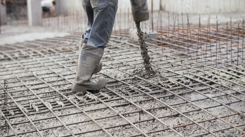 Worker pouring and vibrating concrete on reinforcement at construction site